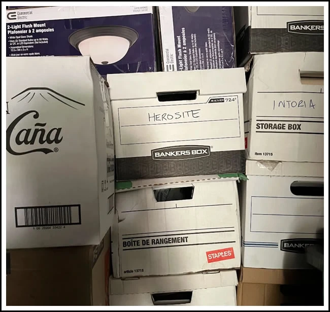 A stack of file boxes in a storage room, the middle one hand-labelled HEROSITE in marker